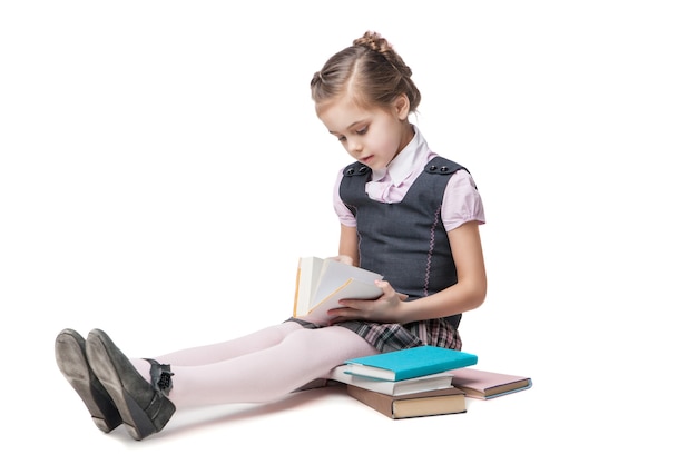 Bella bambina in uniforme scolastica con libri seduta sul pavimento