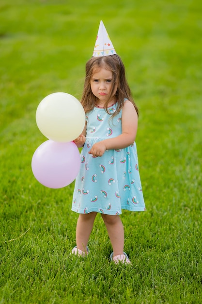 Bella bambina in vestito blu e cappello con palloncini nel parco buon compleanno