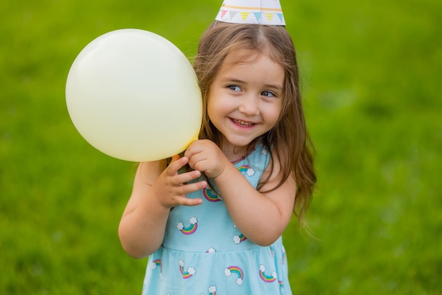 Bella bambina in vestito blu e cappello con palloncini nel parco buon compleanno