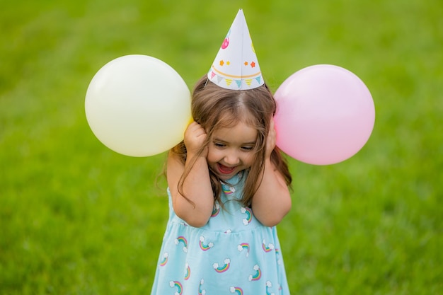 Bella bambina in vestito blu e cappello con palloncini nel parco buon compleanno