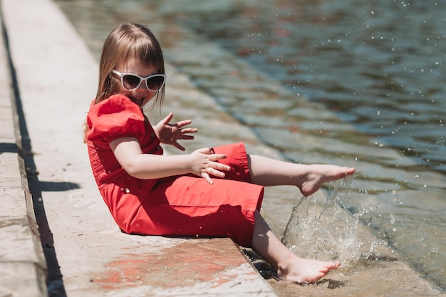 bella bambina in vestito rosso e con gli occhiali che giocano all'aperto con l'acqua