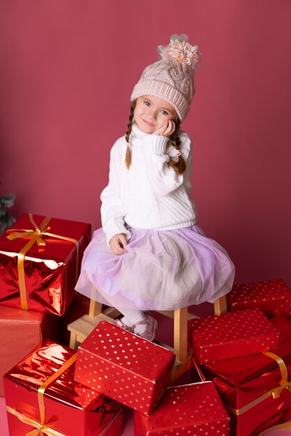 Bella bambina nel cappello che si siede vicino ai regali e all'albero di Natale