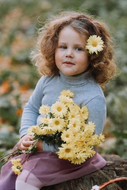 bella bambina riccia in camicia blu nel parco con fiori in autunno tessera sanitaria autunnale