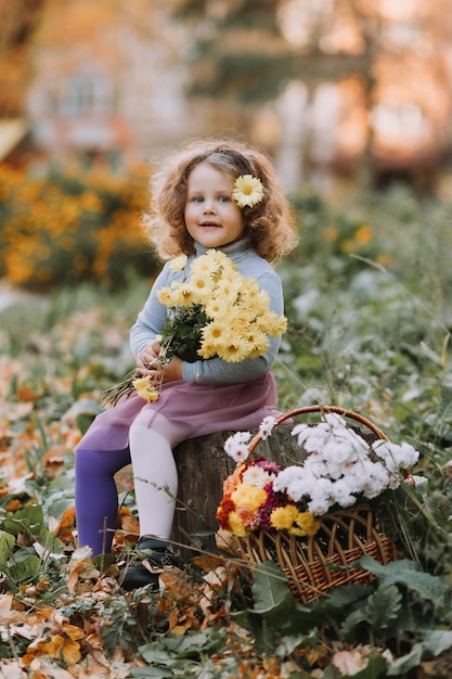 bella bambina riccia in camicia blu nel parco con fiori in autunno tessera sanitaria autunnale