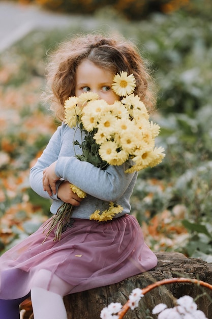 bella bambina riccia in camicia blu nel parco con fiori in autunno tessera sanitaria autunnale