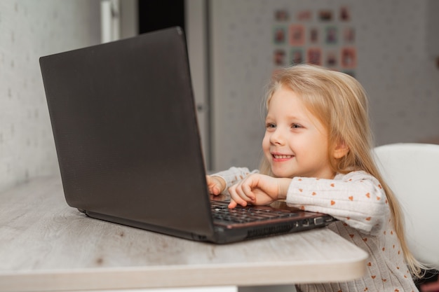 bella bambina seduta a un tavolo con un computer portatile