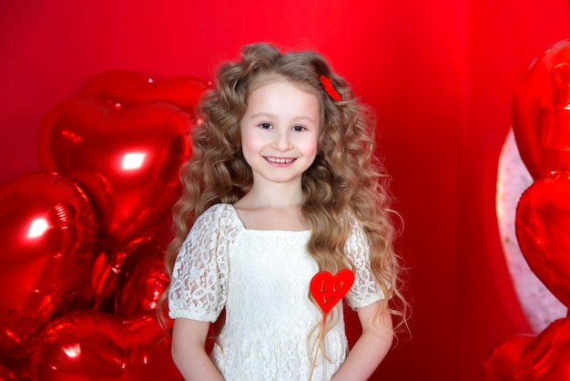 Bella bambina sorride su uno sfondo rosso con un palloncino a forma di cuore e una confezione regalo in mano Il concetto di regali d'amore San Valentino 14 febbraio 8 marzo festa della mamma