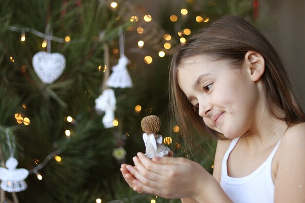 Bella bambina sorridente che decora l&#39;albero di Natale e che tiene la bambola di angelo in mano