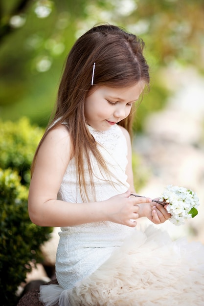 Bella bambina sorridente in abito color crema, contro il verde del parco estivo