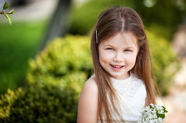 Bella bambina sorridente in abito color crema, contro il verde del parco estivo