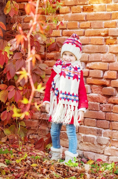 Bella bambina su sfondo vecchio muro di mattoni in autunno