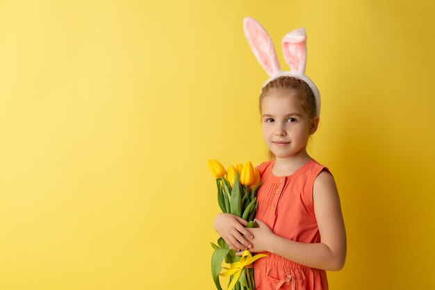 Bella bambina sveglia nelle orecchie del coniglietto di Pasqua che sorride e tiene il mazzo della molla dei tulipani