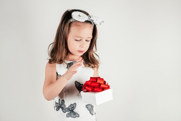 Bella bambina tenere casella presente con arco guardando verso il basso Ritratto di bambino su bianco Concetto di San Valentino