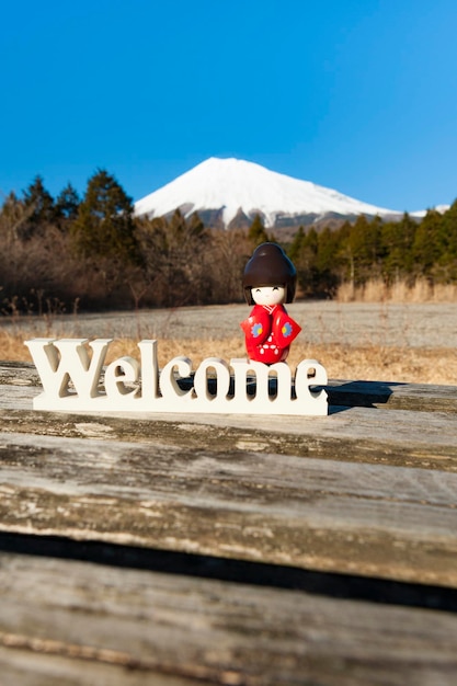 Bella bambola kokeshi tradizionale giapponese vestita con un kimono rosso sopra la parola Welcome