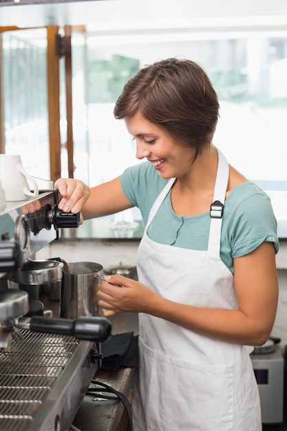 Bella barista fumante brocca di latte alla macchina per il caffè