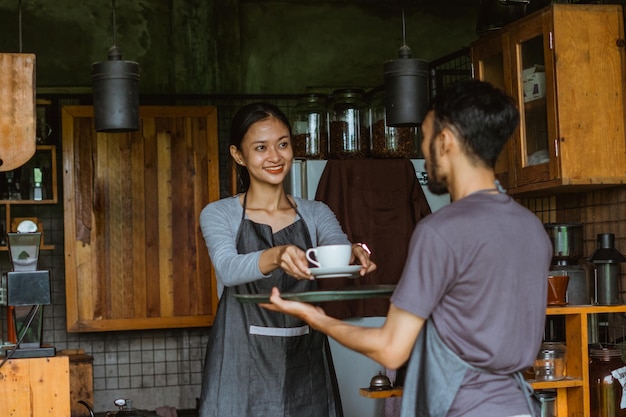 Bella barista in grembiule mise la tazzina di caffè sul vassoio che reggeva il cameriere fuori dal b