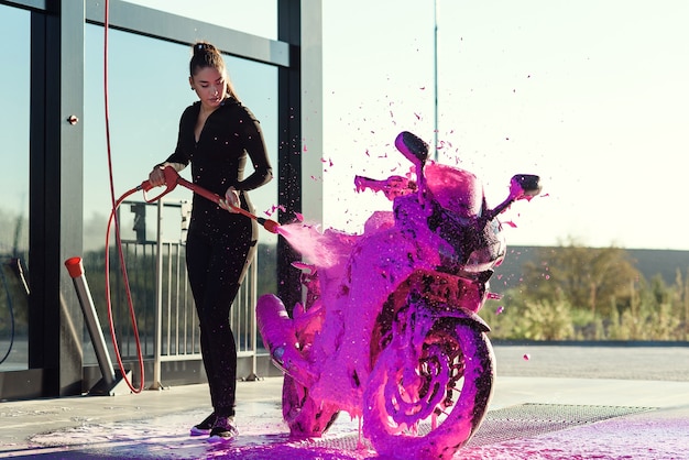 Bella bella ragazza in abito seducente aderente lava una moto all'autolavaggio self-service