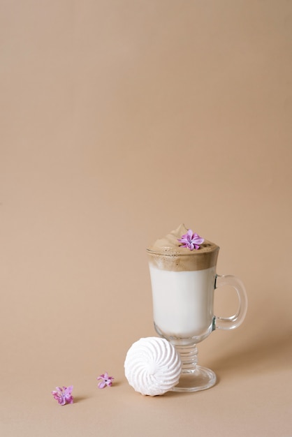 Bella bevanda al caffè dalgon con schiuma in una tazza trasparente e marshmallow su fondo beige. Copia spazio