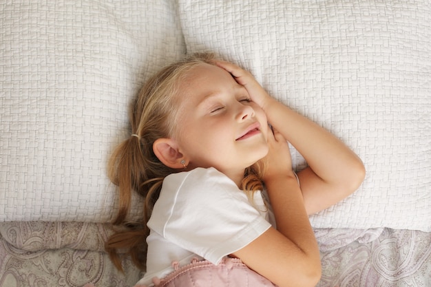 bella bimba bionda con una maglietta bianca dorme a casa sotto una coperta rosa