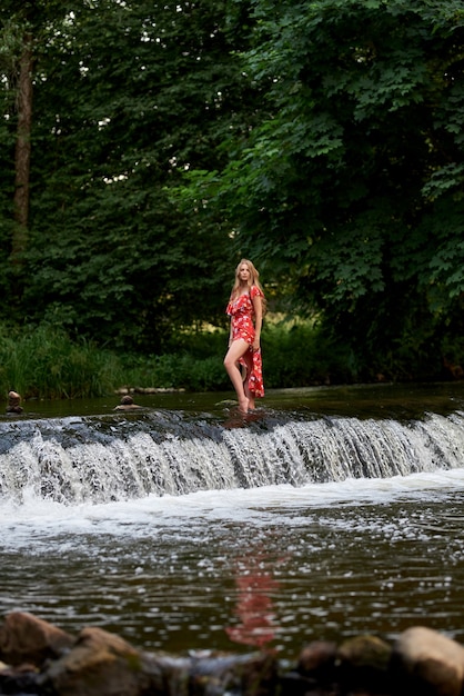 Bella bionda felice in un vestito estivo e un cappello di paglia sta nell'acqua