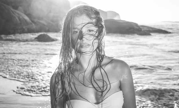 Bella bionda in bikini bianco in spiaggia con i capelli bagnati