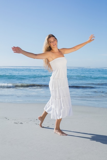 Bella bionda in prendisole bianche sulla spiaggia sorridere alla telecamera