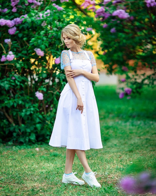 Bella bionda in un vestito bianco all'aperto tra i lillà