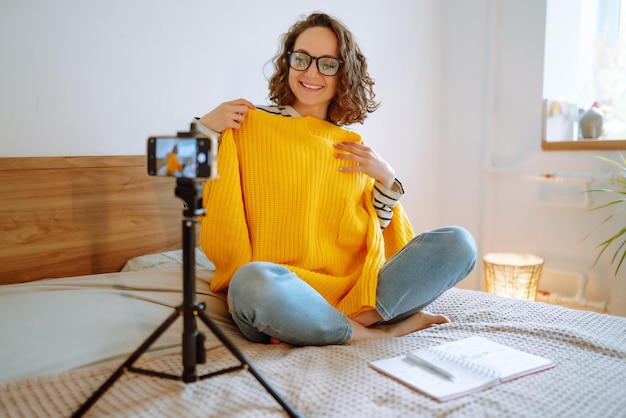 Bella blogger di moda che tiene un maglione giallo che registra sognante video per vlog Marketing online