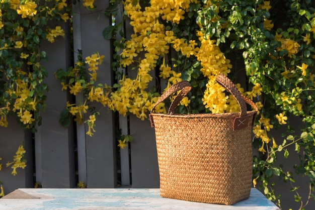 Bella borsa di vimini intrecciata sulla tavola di legno blu con i fiori gialli freschi