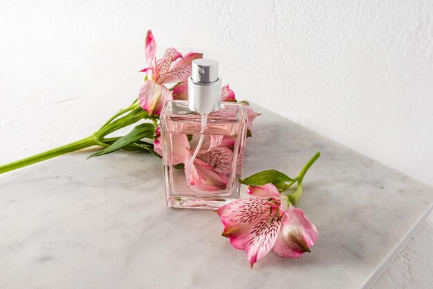 Bella bottiglia di profumo o spray da donna sullo sfondo di fiori rosa e lastra di marmo bianco presentazione della vista dall'alto dell'aroma