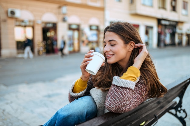 Bella bruna bere caffè sulla panchina della città.