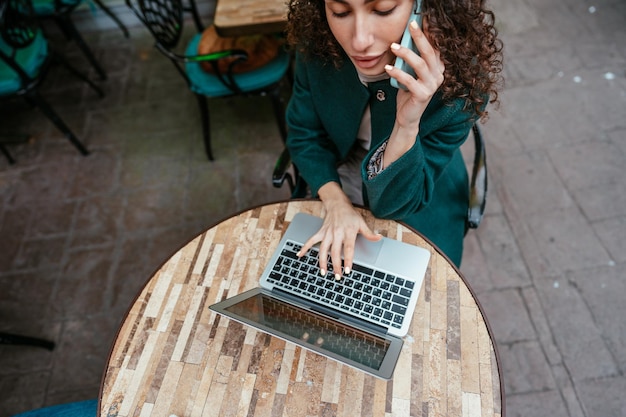 Bella bruna che usa il portatile e parla al telefono in un caffè.