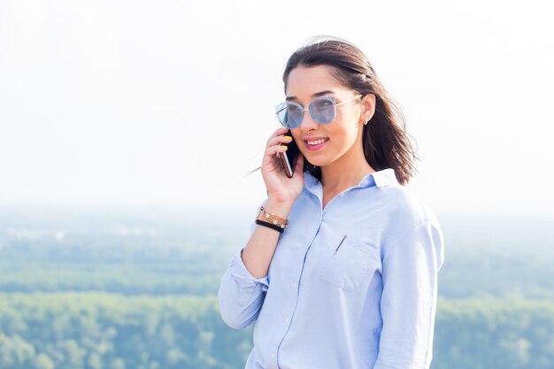 Bella bruna donna d'affari felicemente parlando su uno smartphone in natura in estate