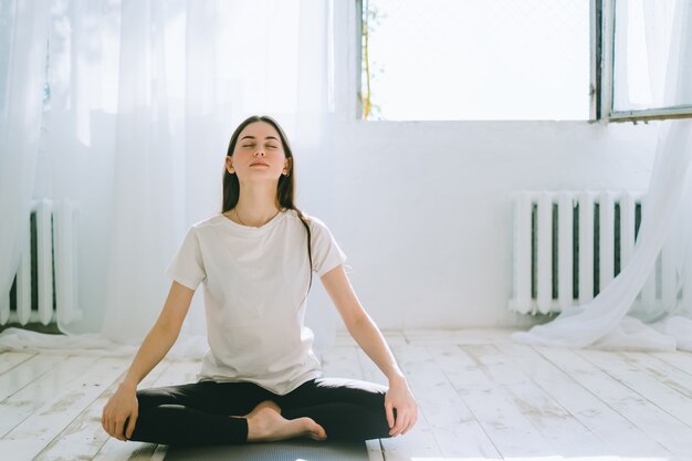 Bella bruna fitness donna medita, facendo yoga al chiuso a casa