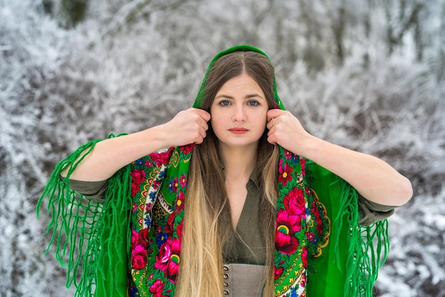 Bella bruna in abito verde e scialle in piedi in una foresta d'inverno.