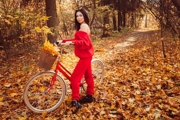 Bella bruna nella foresta di autunno con una bicicletta