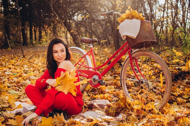 Bella bruna nella foresta di autunno con una bicicletta