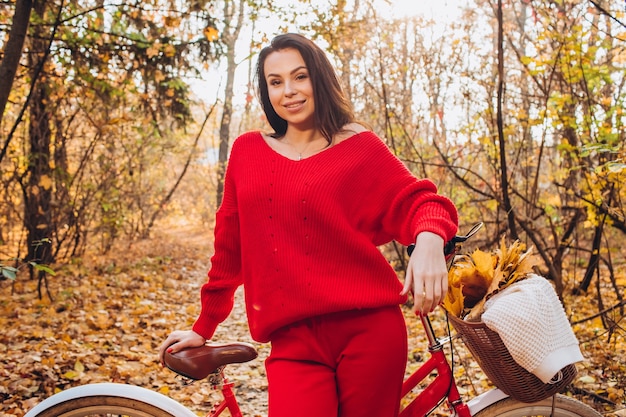 Bella bruna nella foresta di autunno con una bicicletta