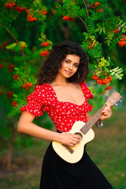 Bella bruna ragazza riccia in costume zingaro rosso che suona la chitarra