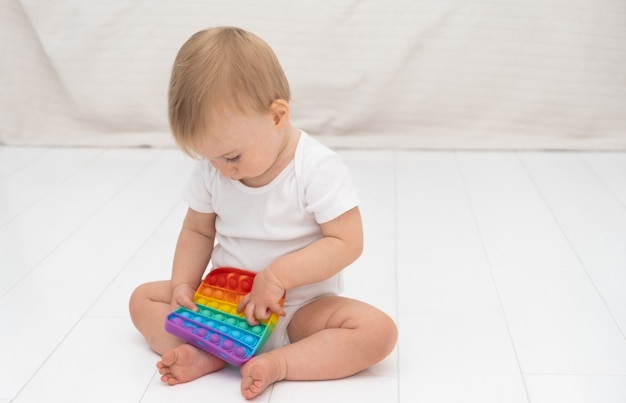 Bella carina caucasica interessata bambina seduta sul pavimento a casa a giocare con il gioco popit sullo sfondo di un divano luminoso interno moderno Concetto di sviluppo del bambino