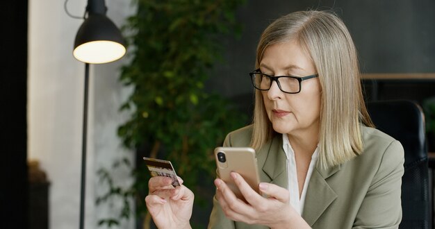 Bella carta di credito senior della tenuta della donna di affari e comperare online sullo smartphone.