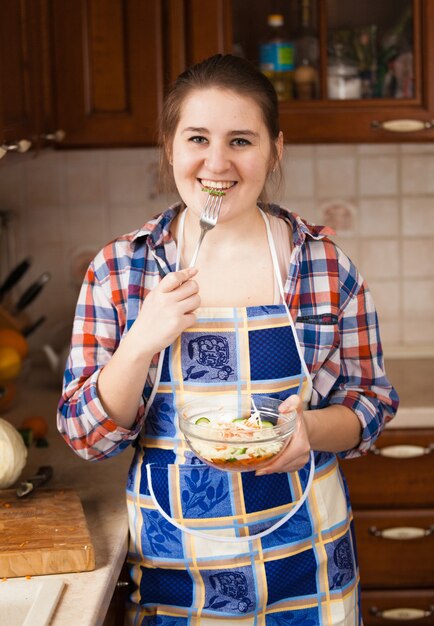 Bella casalinga sorridente che mangia insalata in cucina