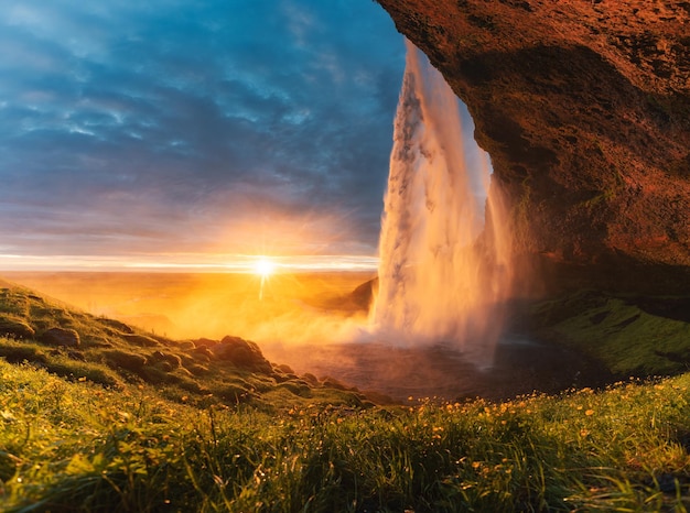 Bella cascata Seljalandsfoss che scorre e tramonto di mezzanotte che brilla sul giardino fiorito in estate in Islanda