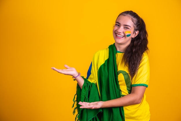 Bella cheerleader brasiliana con la faccia dipinta che indica di lato sullo spazio libero per il testo Il tifoso brasiliano indica di lato