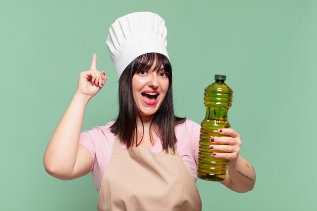 Bella chef donna che celebra con successo una vittoria e tiene in mano una bottiglia di olio d'oliva