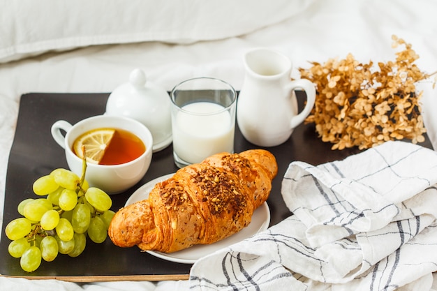 Bella colazione con un croissant e tè su un vassoio nero sul letto.