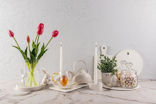 Bella composizione festiva per le vacanze di Pasqua su un bancone di marmo di candele di cucina luminose un vaso di tulipani uova di Pasqua e conigli