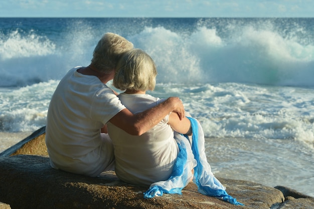 Bella coppia anziana felice che si siede sulla spiaggia al resort tropicale