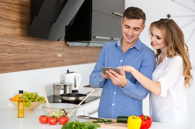 Bella coppia che utilizza smartphone e cucina in cucina a casa