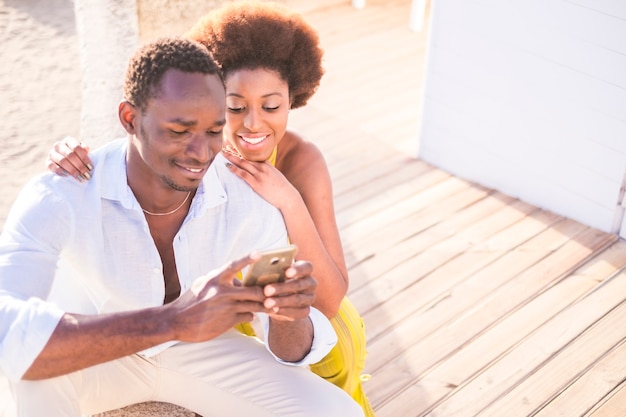 bella coppia di modelli africani di razza nera usa lo smartphone insieme in amicizia sorridendo e godendosi il contenuto. connesso con gli amici o guardando le foto. concetto di coppia di amici d'amore